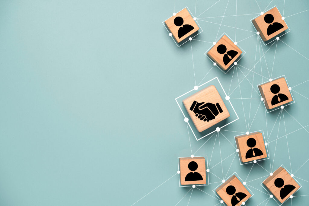 Top view design on blue background of hand shaking imprint on wooden block with lines connecting to other wooden blocks with imprints of people icons