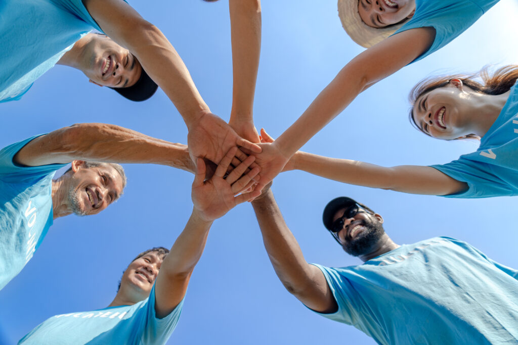 Group of happy diverse volunteers joining stacked hands together with smiles