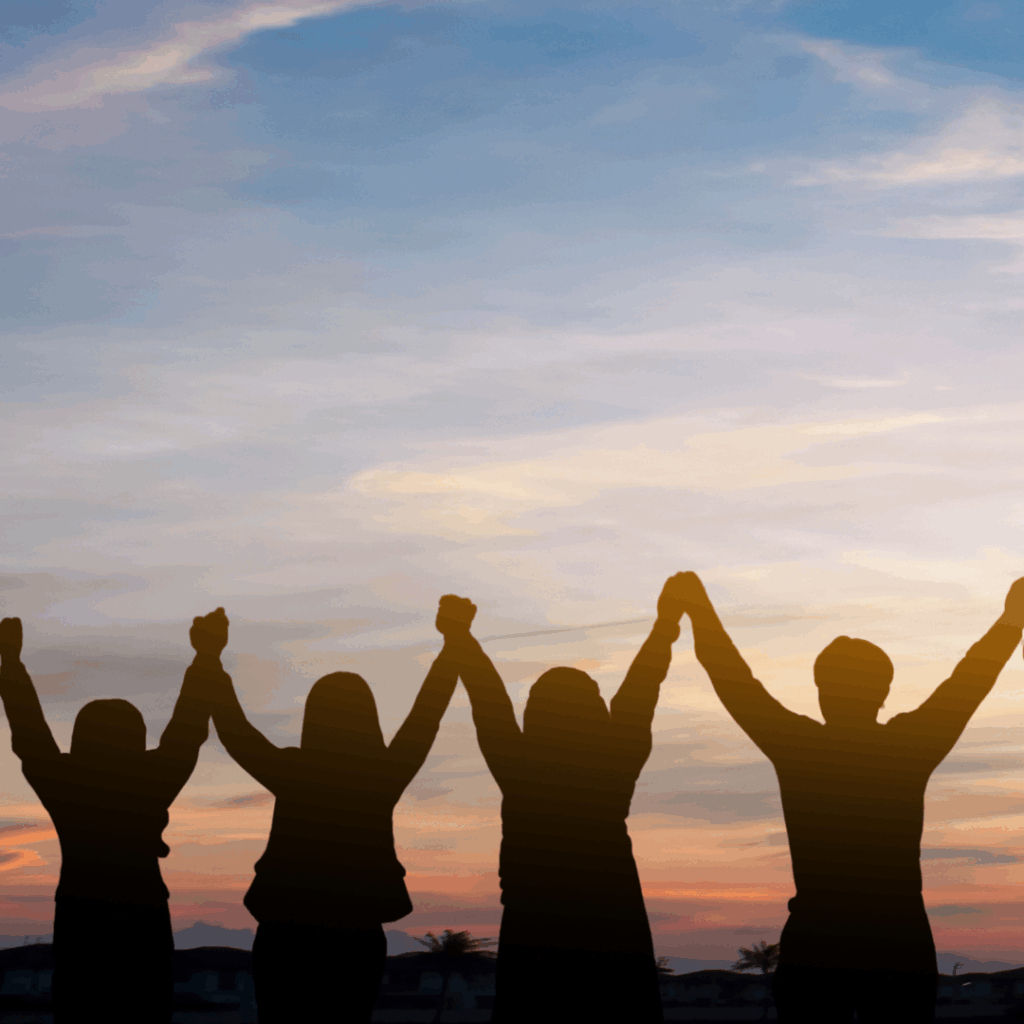 Silhouette of group holding hands over head in sunset sky
